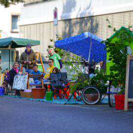 Entspannt sitzen die Aktiven des PARK(ing) DAYs auf Stühlen auf umgestalteten Parkplätzen mitten in der Innenstadt. Im Vordergrund ein Schild: PARK(ing) DAY - heute ist Böblingen schöner