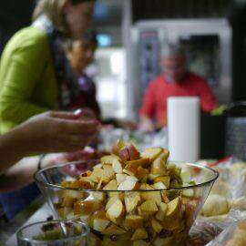 Fleißige Hände bereiten einen Obstsalat bei der Schnippeldisco zu, im Hintergrund andere Schnippler